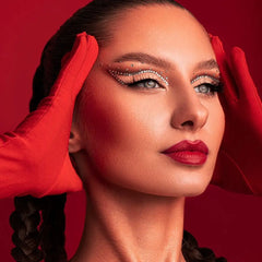 Une femme portant des gants en satin rouge, encadrant son visage avec ses mains sur un fond rouge uni.