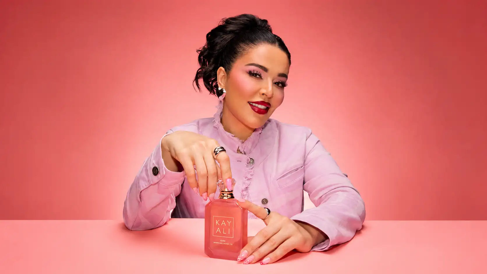 Flacon de parfum en verre rectangulaire rose avec lettrage doré et un bouchon doré assorti, portant la marque kay ali